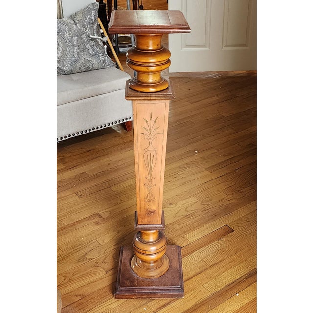 A slender wood pedestal stand with a turned bulbous and tapered shaft incised with a stylized urn and foliate motif. No...
