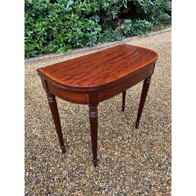 A Regency Mahogany D-Shaped Card Table with Rosewood inlay and banding on turned reeded tapered legs. The two back legs...