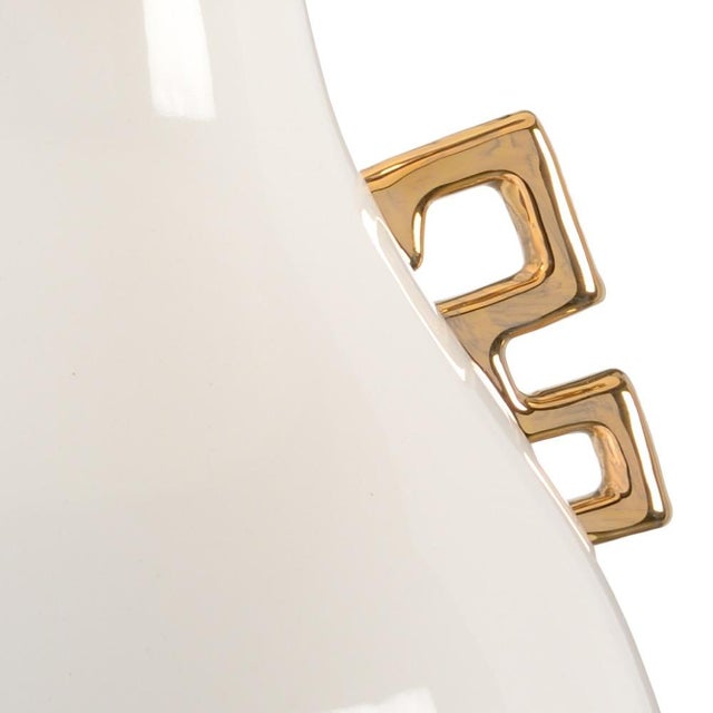 Metallic gold handles accent a large pear shaped white glazed ceramic vase with a square gold leaf base. Capped off with a...