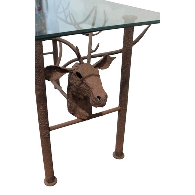 A vintage iron table featuring two stags with sculptural intertwined antlers and a glass top.