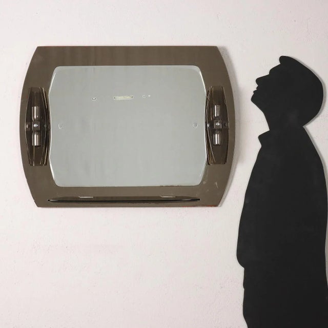 Wall mirror, with shelf and side appliques. Mirrored glass and smoked glass. This piece is attributed to the mentioned...