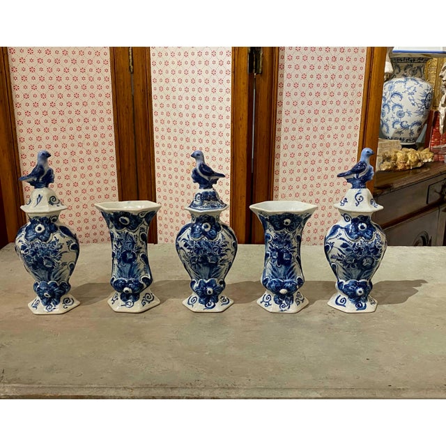 A five piece Delft 18th century garniture set with bird finials. Marked with three bells. 11” High With Lid, 7” High Without