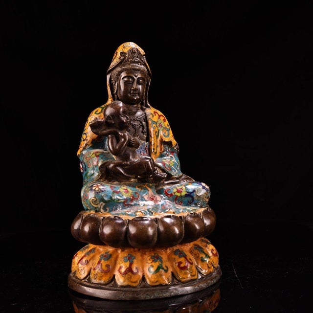 This is a finely cast bronze figurine of Guanyin (the Bodhisattva of Compassion) seated with a child. The deity's face and...