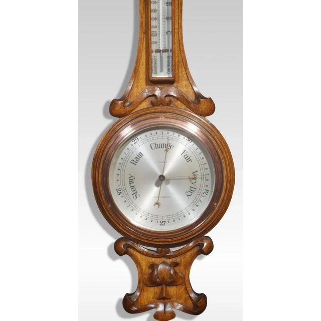 Carved oak barometer, the shaped carved oak frame with rectangular thermometer above the silvered dial inscribed J....