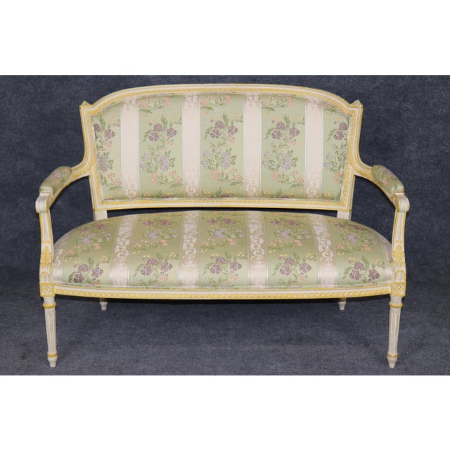 Graceful, refined, and unmistakably elegant, this exceptional French Louis XVI style painted and parcel-gilt settee is a...