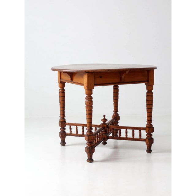 This is an antique accent table. The round pine table features turned legs and decorative stretchers with finial center....