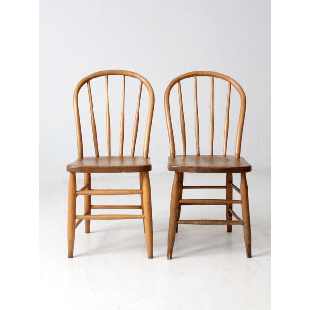 This pair of antique Windsor-style bow back chairs features elegant spindle backs, gently contoured seats, and a warm...