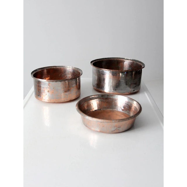 This is a set of three antique copper basin bowls. The hammered copper bowls feature lipped rims and etched stripes on...