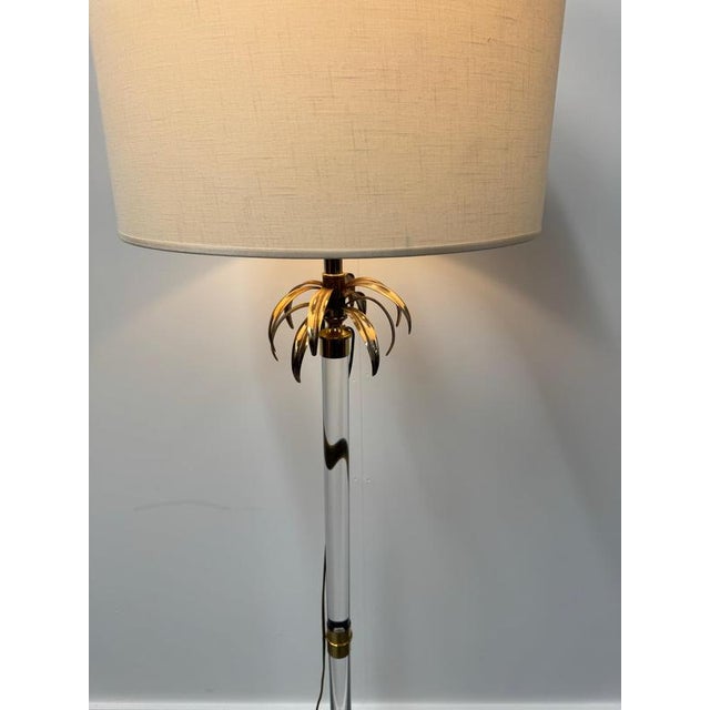An Italian 1970s floor lamp comprising of a long acrylic glass column supported by a circular brass base with brass palm...