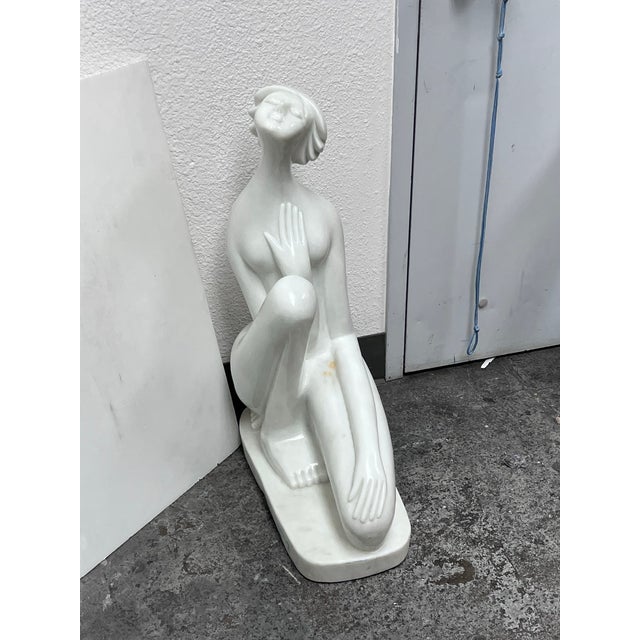 Design Plus Gallery presents a Signed Marble Art Deco Sculpture of a Kneeling Woman. The figure tilts her head upward with...