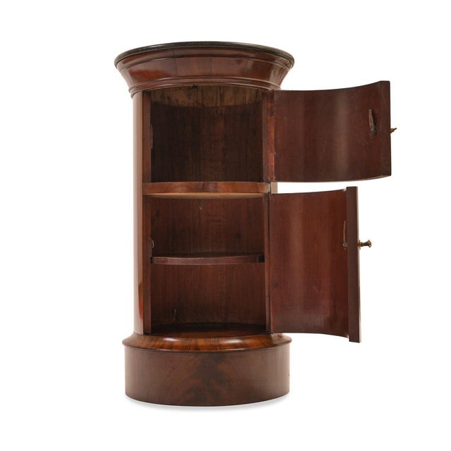 Drum cabinet, France, Empire style, circa 1815, Mahogany, topped with a projecting pedestal, Black marble, two hinged...