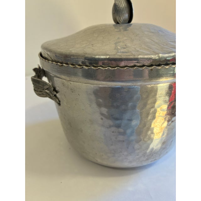 This hammered aluminum lidded container features a tulip-shaped finial and applied Art Nouveau floral handle detailing,...