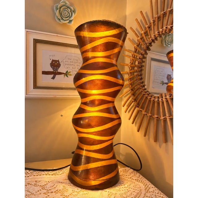 A striking sculptural table lamp featuring a dramatic, undulating hourglass silhouette and flowing ochre-gold stripes...