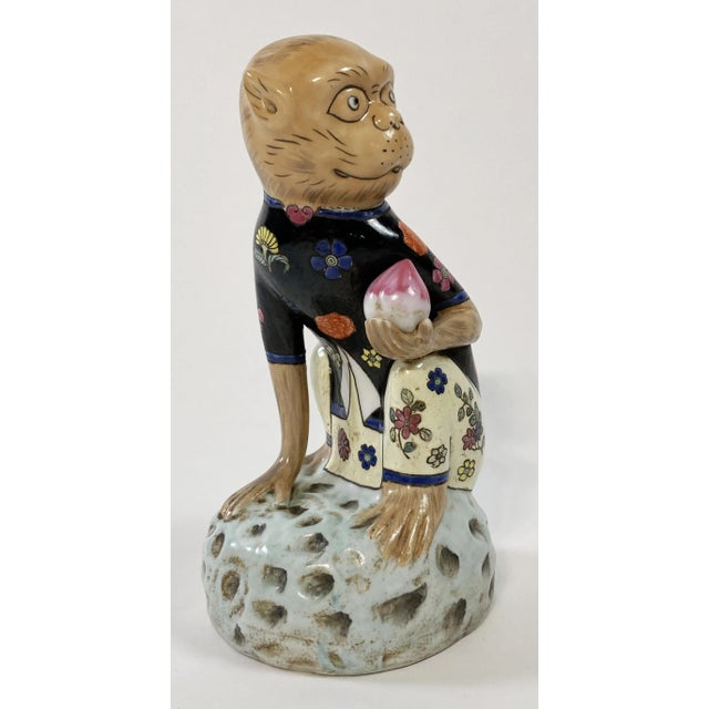 Whimsical vintage Chinese snub nosed monkey sculpture. Monkey is seated on a rock and holding a pink and white plum or...