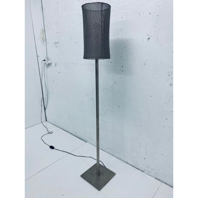 Custom floor lamp fabricated of a tubular steel rod welded to a square base and topped with a metal mesh lamp shade. The...