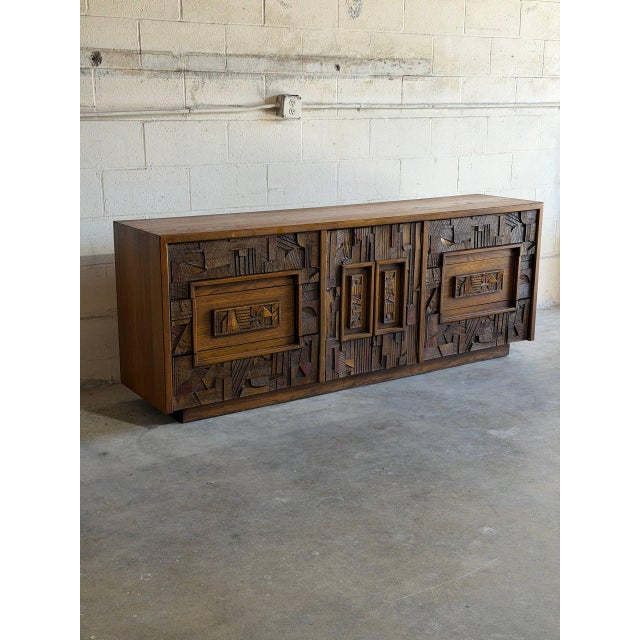 This vintage wooden sideboard features an expansive rectangular profile highlighted by a dramatic three-dimensional...