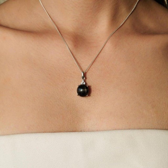 Crafted in 925 sterling silver, this striking pendant showcases a captivating 7.91 carat Black Star gemstone in a classic...