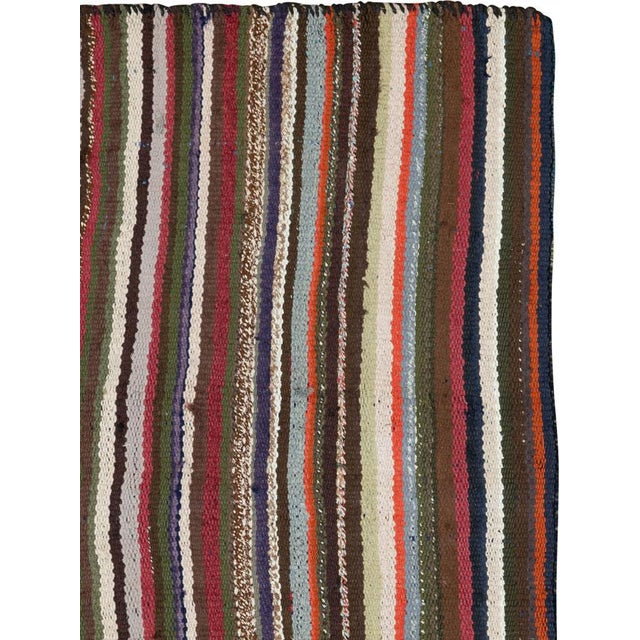This Mid-20th century Persian flatweave kilim presents a refined, vertically striped composition rendered in a rich,...
