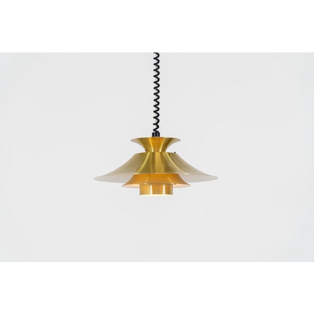 Brass colored pendant light by Frandsen (Denmark, 1970s). A beautiful lamp made out of four aluminium shades with a brass...