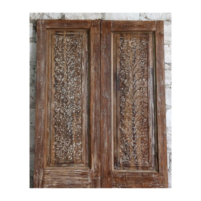 These striking antique double doors feature intricate hand carving and authentic brass stud detailing, showcasing the...