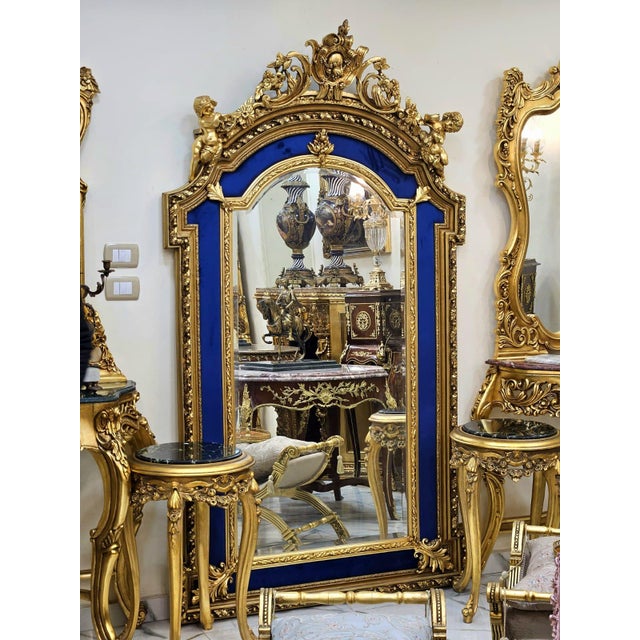 An extraordinary French Baroque style wall mirror featuring a richly carved gilded frame accented by striking royal blue...
