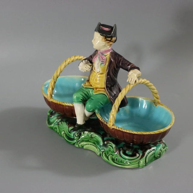 Minton Majolica dish which features a young male vintager, sat between two baskets. Colouration: brown, green, yellow, are...