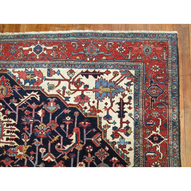 An early 20th-century traditional navy blue and brown accent, ivory field room size Persian Heriz carpet. Measures: 9' x...