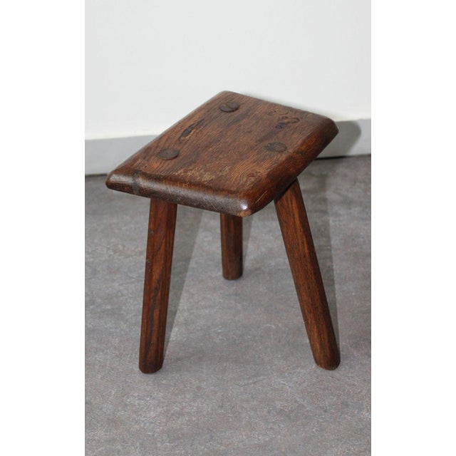 This handcrafted tripod stool in solid wood, with a brutalist design, has a sturdy hexagonal seat with rounded edges...