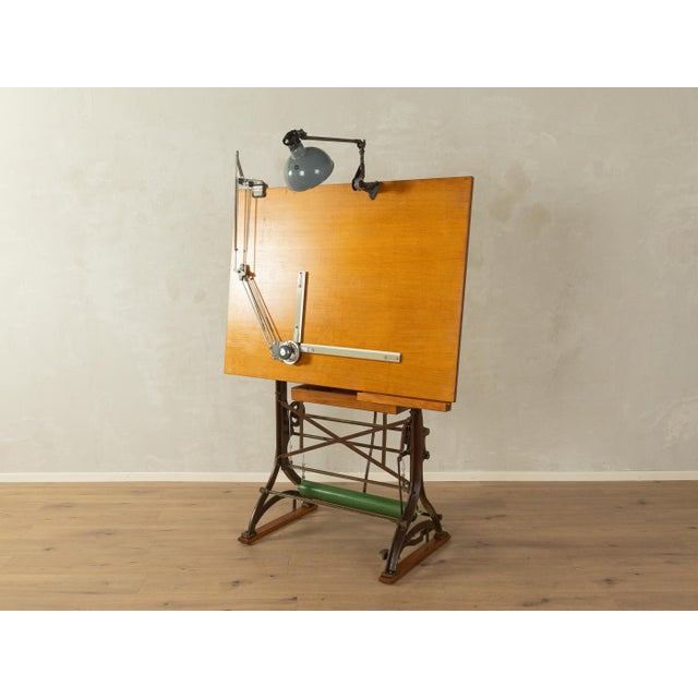 Unique drafting table from the 1920s. High-quality steel construction with a wooden drawing board and shelf, and a lamp....