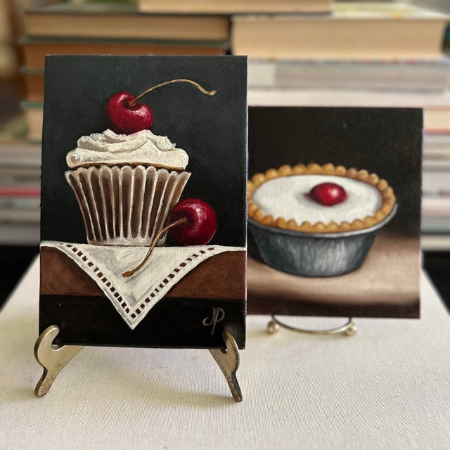 Pair of original dessert still life paintings by Jane Palmer, each featuring a richly painted cherry-topped pastry against...