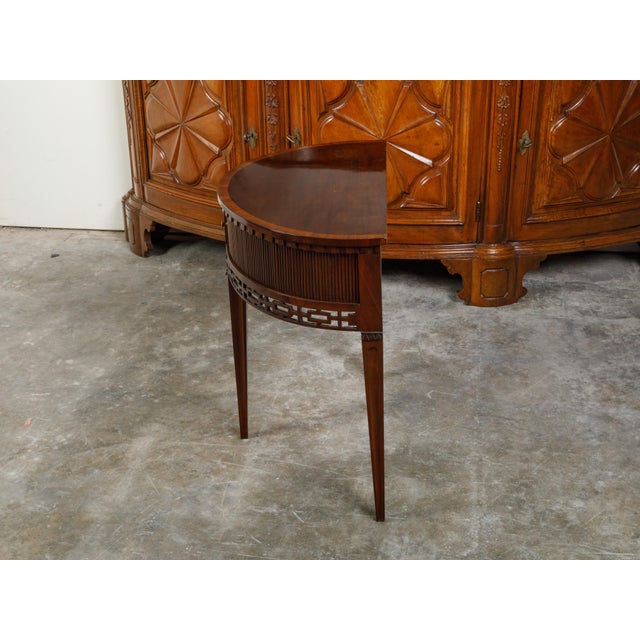 An English mahogany demi-lune console table from the 19th century, with a dentil cornice over two reeded tambour sliding...