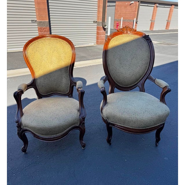 Coordinated pair of Victorian-style parlor armchairs featuring carved wooden frames, curved arms, padded armrests, and...
