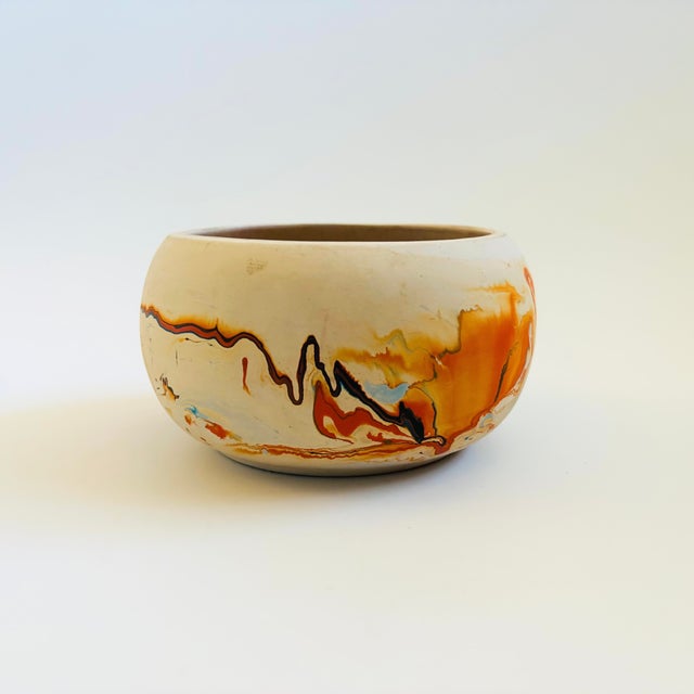 A vintage nemadji pottery bowl with a beautiful organic pattern of blue and orange swirls on a light off-white background....