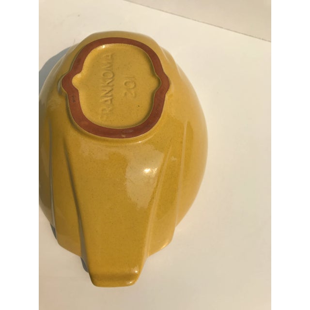 This glazed clay bowl is designed in an oval shape with gentle fluting on the ends. The color is a warm yellow with brown...