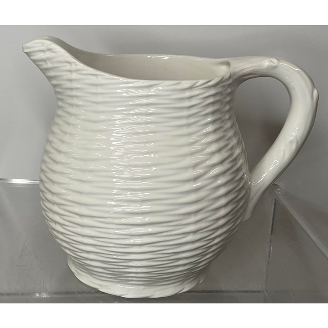 Ceramic pitcher with woven basket motif. Woven basket weave featured on exterior of pitcher including base. Makers mark is...