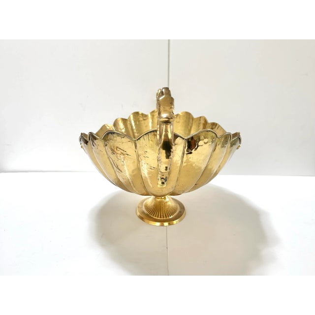 A dramatic large-scale Hollywood Regency brass pedestal bowl featuring a scalloped rim, ornate scroll handles, and a...