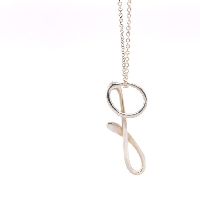 A delicate Tiffany & Co. Elsa Peretti Small “G” Alphabet pendant necklace crafted in sterling silver, featuring Peretti’s...