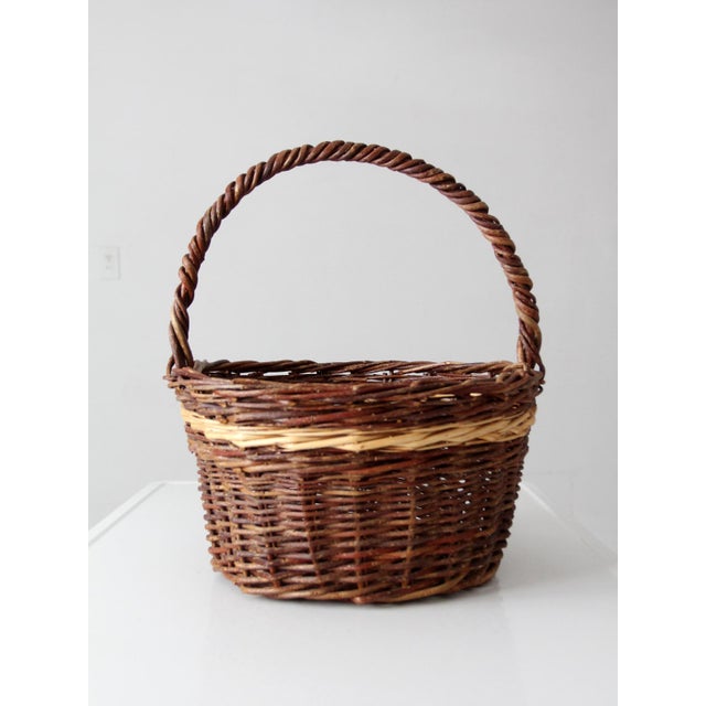 A vintage wicker gathering basket in a rich mix of natural tones, with a softly time-worn patina that adds depth and...