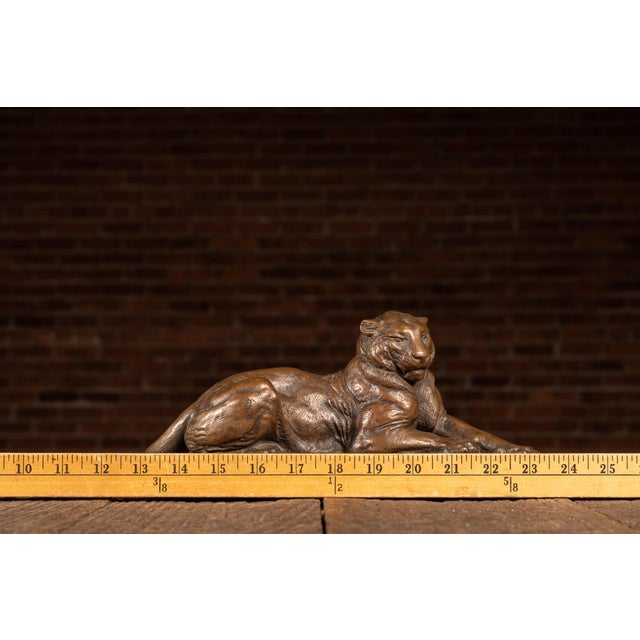 Bronze-clad resin sculpture depicting a reclining tiger posed at rest atop a textured naturalistic base. The figure is...
