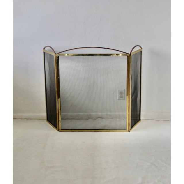 This vintage three-panel fireplace screen features a polished brass frame and a black protective mesh guard. Folding hinge...
