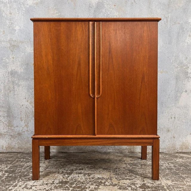 a compact teak drinks cabinet with sculpted wooden handles and a raised four-leg frame. Details danish attribution, circa...
