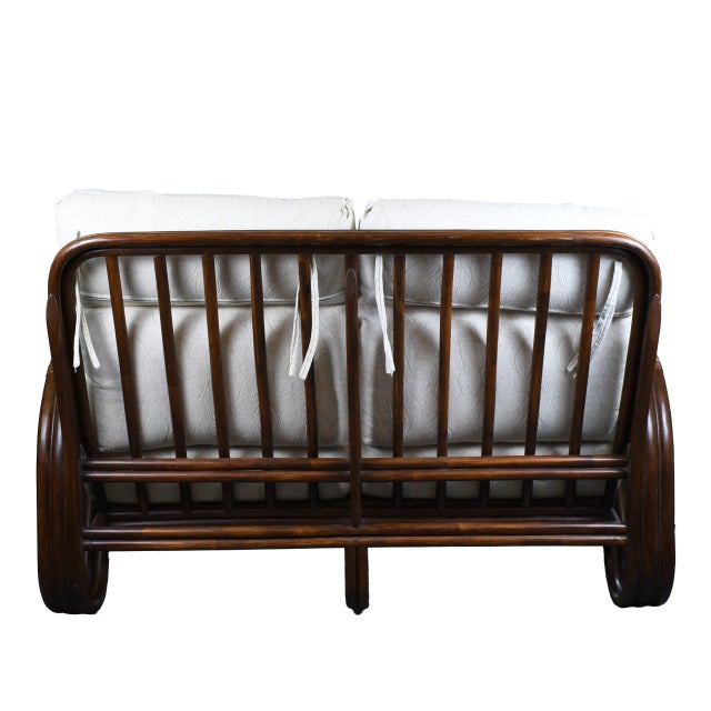 A pretzel rattan settee, its frame bent into the curled, ribbon-like loops that give pretzel rattan its name. The open,...