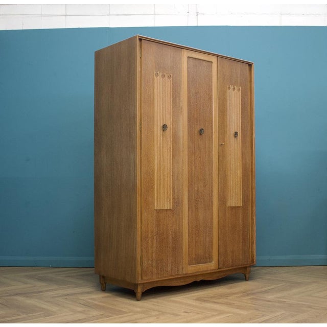 1950s limed oak wardrobe with carved vertical panels and metal handles, raised on shaped feet with a curved base. Central...