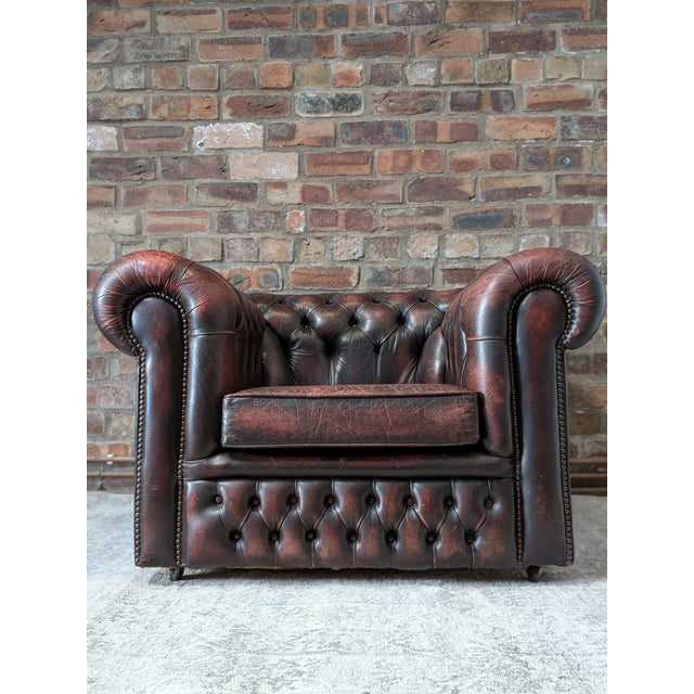 A classic deep‑buttoned Chesterfield armchair in rich patinated oxblood leather with caster feet and decorative brass nail...