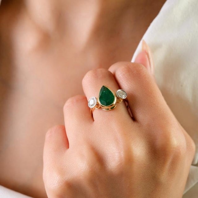 This elegant three-stone ring features 1 natural pear-shaped emerald totaling 2.29 carats, set in 18k yellow gold. The...