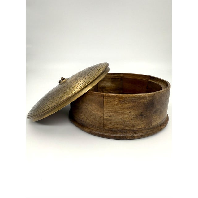 A beautifully handcrafted round storage box featuring a warm mango wood base topped with an intricately etched brass dome...