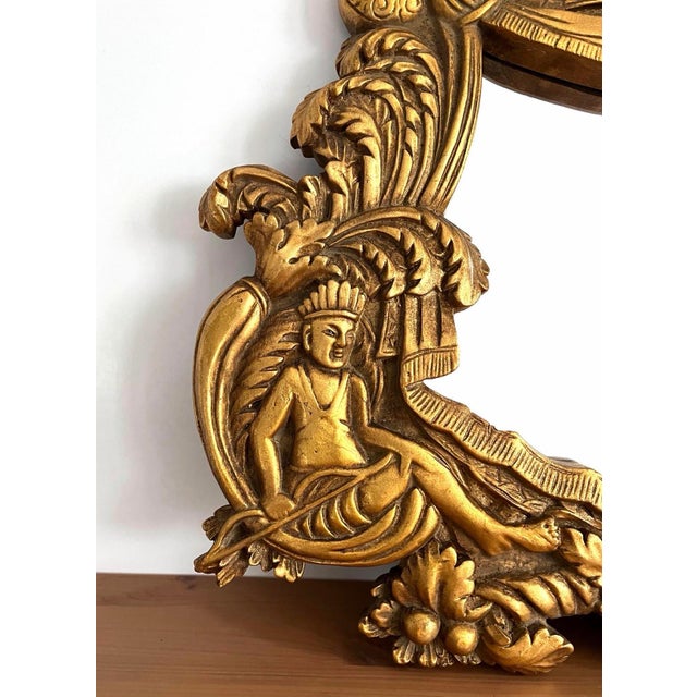 A mid century carved wood mirror in gilt finish. Ornate Rococo style with two native Islander figures. There is one crack...