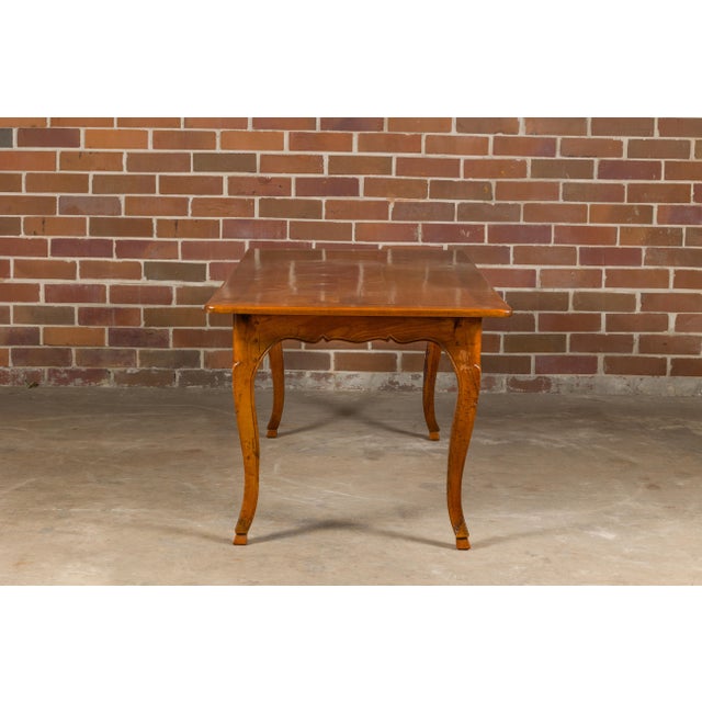 A rustic French Louis XV style fruitwood farm dining table from the 19th century with bread board, cabriole legs, carved...