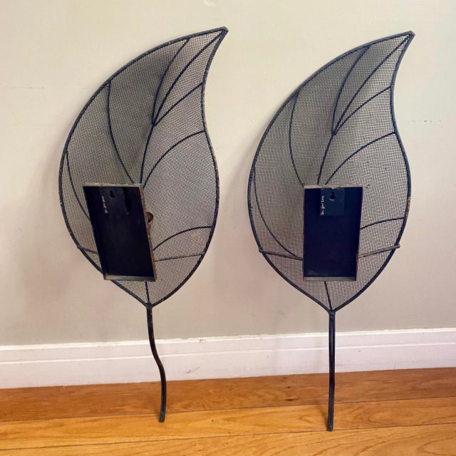 The sconces utilize a woven metal wire mesh framed by sculpted iron or steel rods, mimicking natural leaf veins and a...
