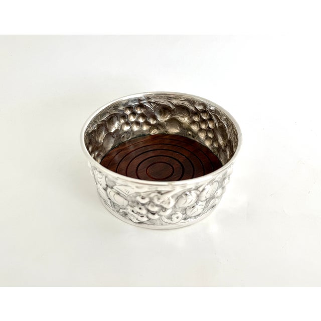 This ornate English silverplate wine coaster features a repousse design of grapes and leaves and a wood liner to the...